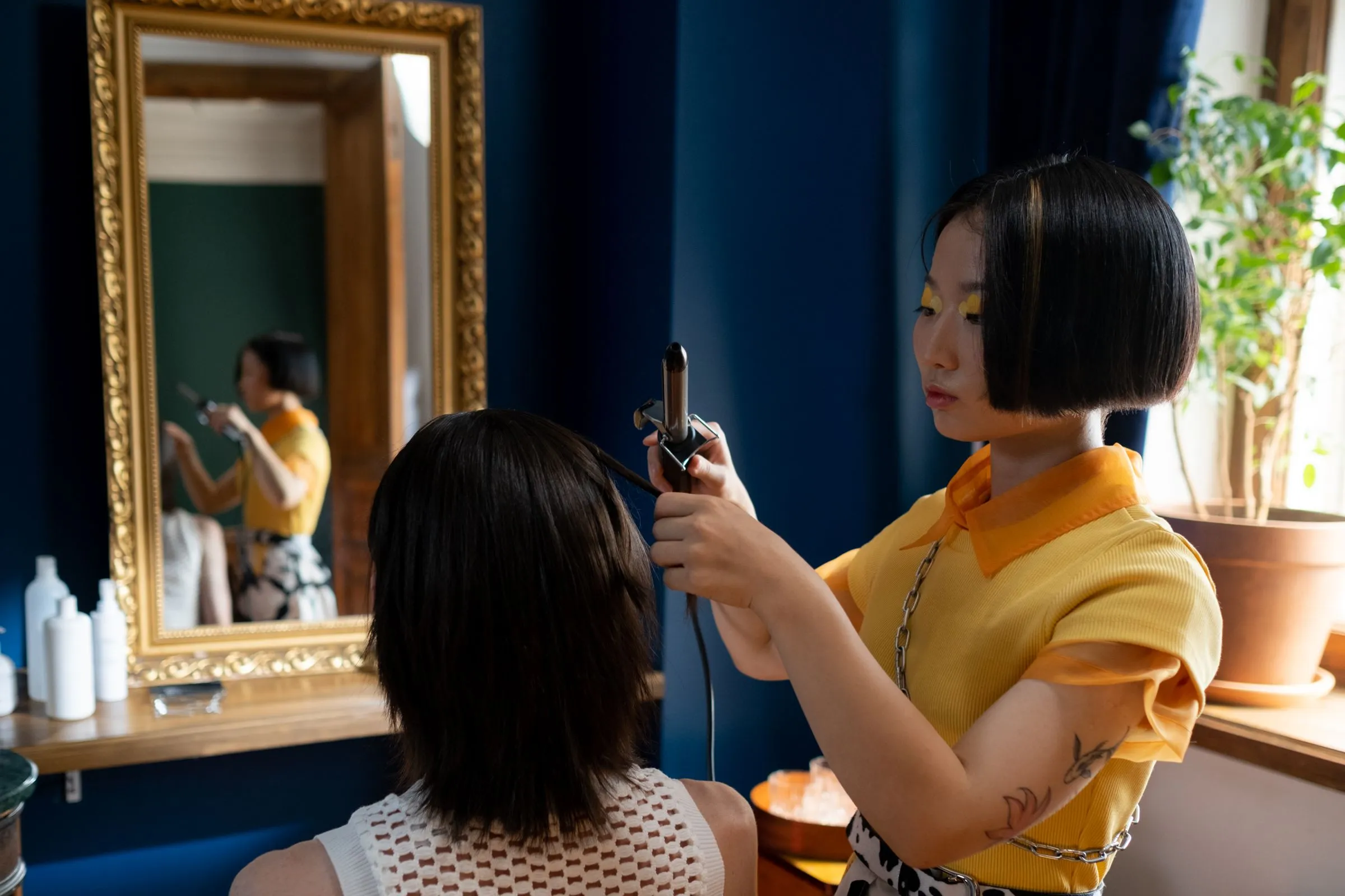 Friseurin stylt die Haare einer Kundin mit einem Lockenstab in einem hellen Salon